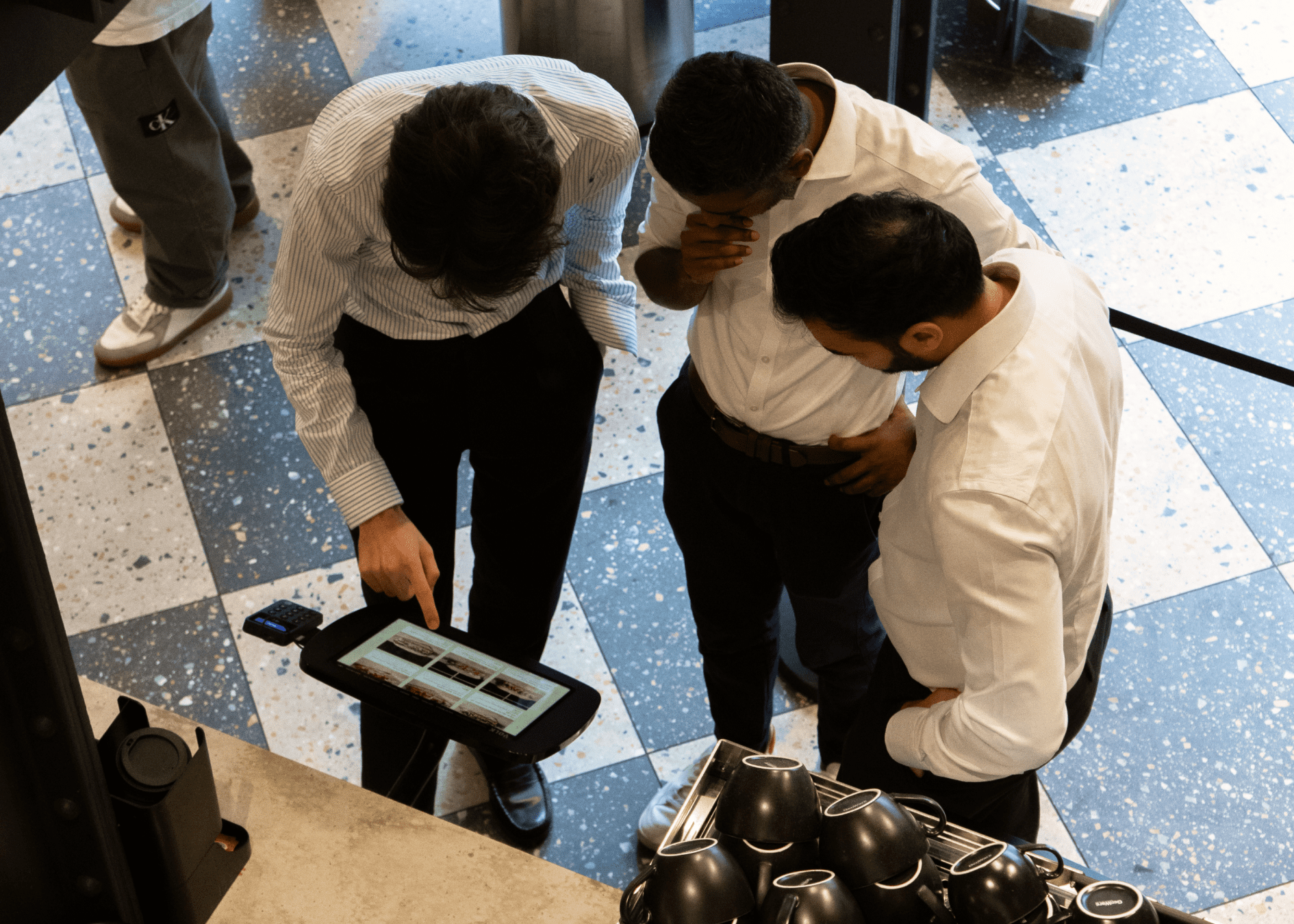 Three men in shirts gathered around a kiosk ordering food